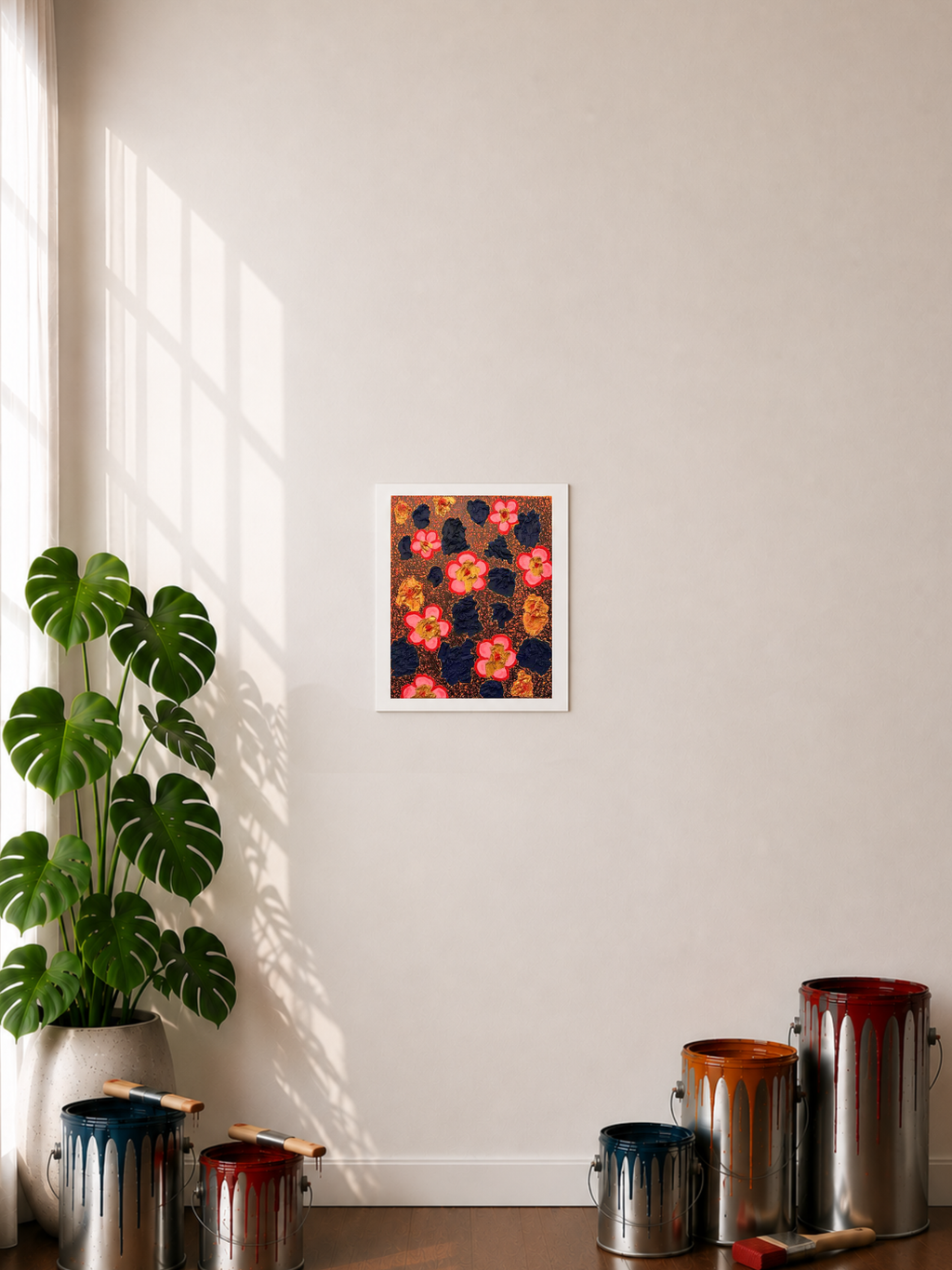 A paper print with a .5-inch white border featuring an abstract art piece displayed on a wall in a styled room with a plant, paint cans, and window shadows in the display. The art image has blue abstract clusters laying on top of an orange background with black abstract line art. There are also gold-colored abstract clusters that have a red dot stroke like accent in the middle of each cluster. Another element is the pop art pink flowers with a red border on the petals and a gold core with a red dot.